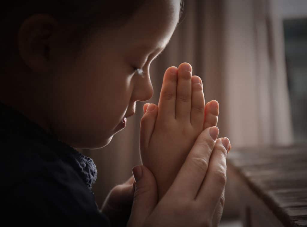 Religious Christian girl praying with her mother indoors, symbolizing how human development plays into culture