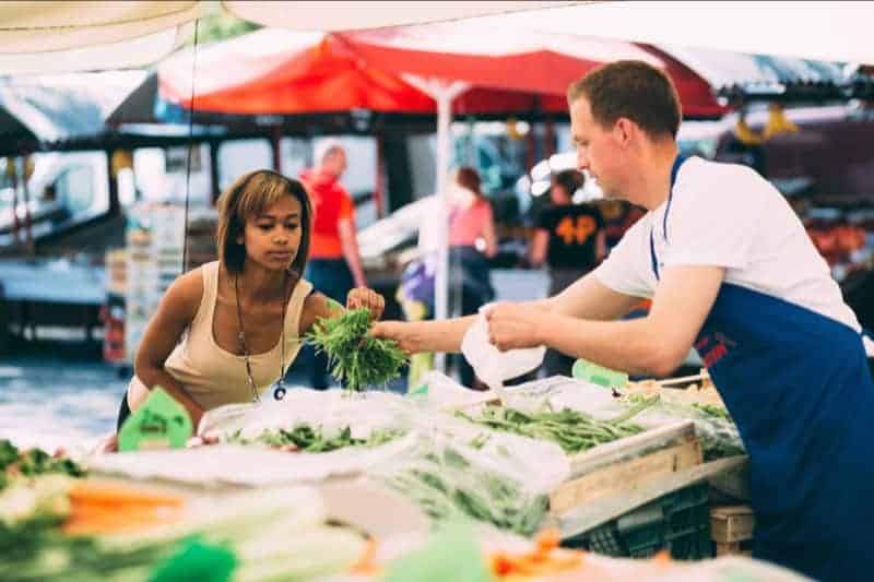 A man at an outdoor marketplace hands chives to a woman, showing how the right to private property supports the common good