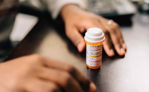 Someone leans against a counter on which a bottle of medicine rests, calling to mind the preferential option for the poor in the case of the moral poor
