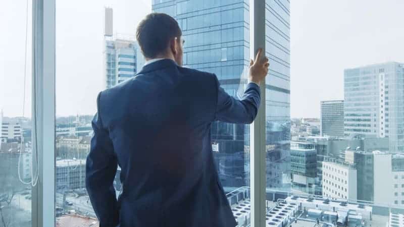 A man in a suit looks out of an office window, presumably contemplating the preferential option for the poor