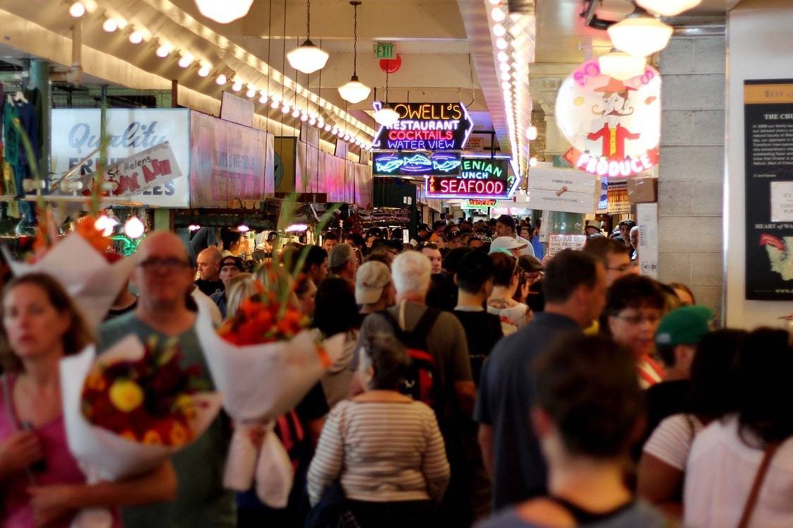 A crowd of shoppers in a gaudy mall shows the pathology of excessive consumption, which has a bad effect on the physical environment
