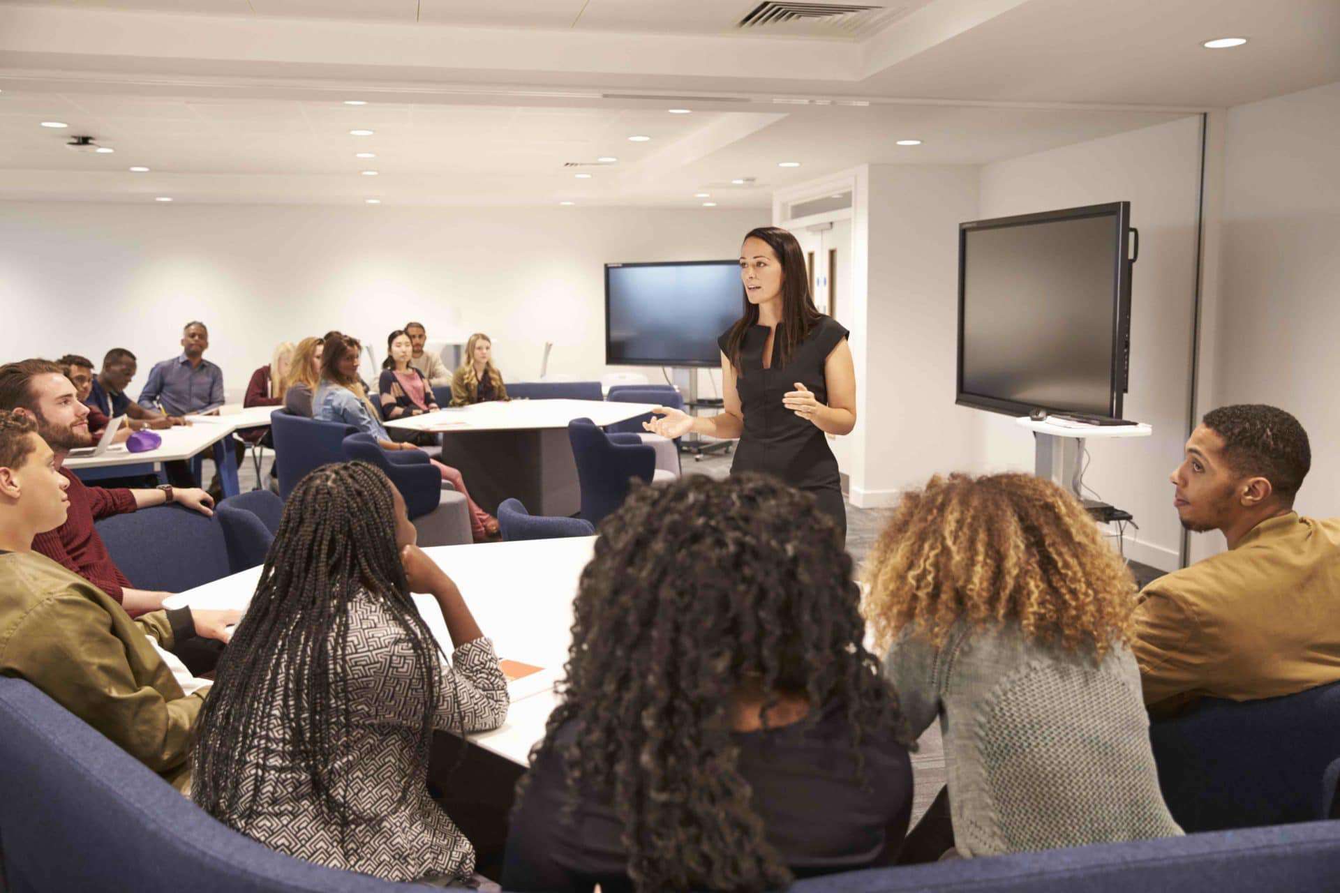 A woman stands in a modern conference room speaking to twelve or fifteen people, showing the structural change that will be necessary to preserve the human environment