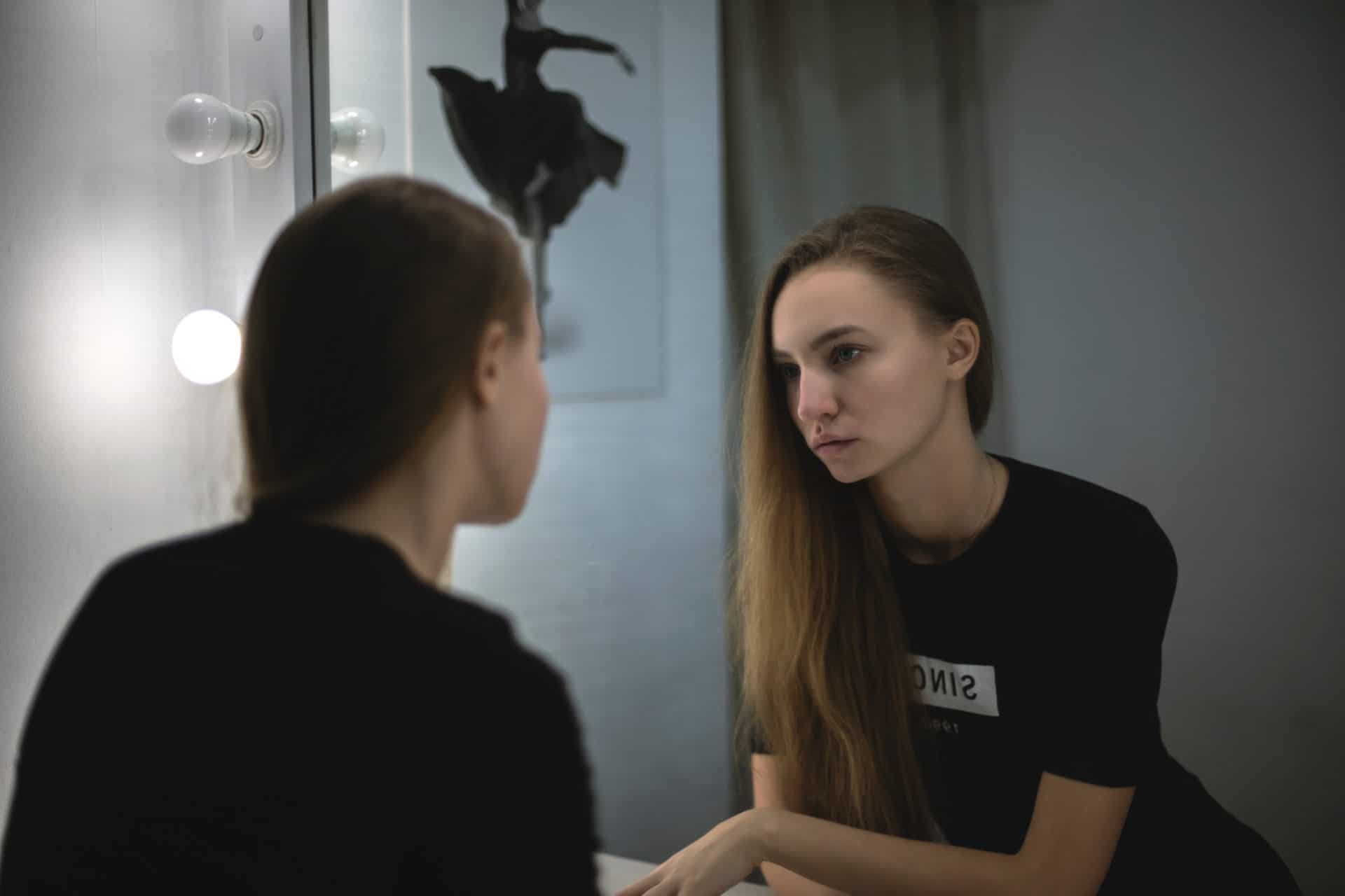 A young woman stares at herself in a bathroom window, symbolizing the need for personal conversion in order to preserve the human environment
