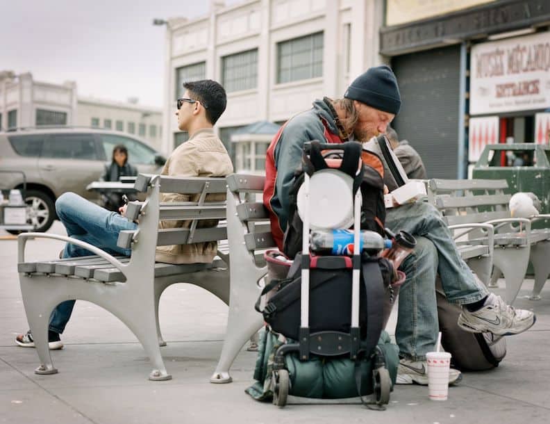 People walk along a city street surrounded by billboards, showing the effect of consumerism on society as a whole