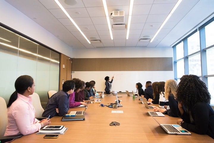 boardroom-business-meeting-coworkers-colleagues-company-discussion-whiteboard-conference-profits-headquarters Company employees gather for a business meeting in a conference room.